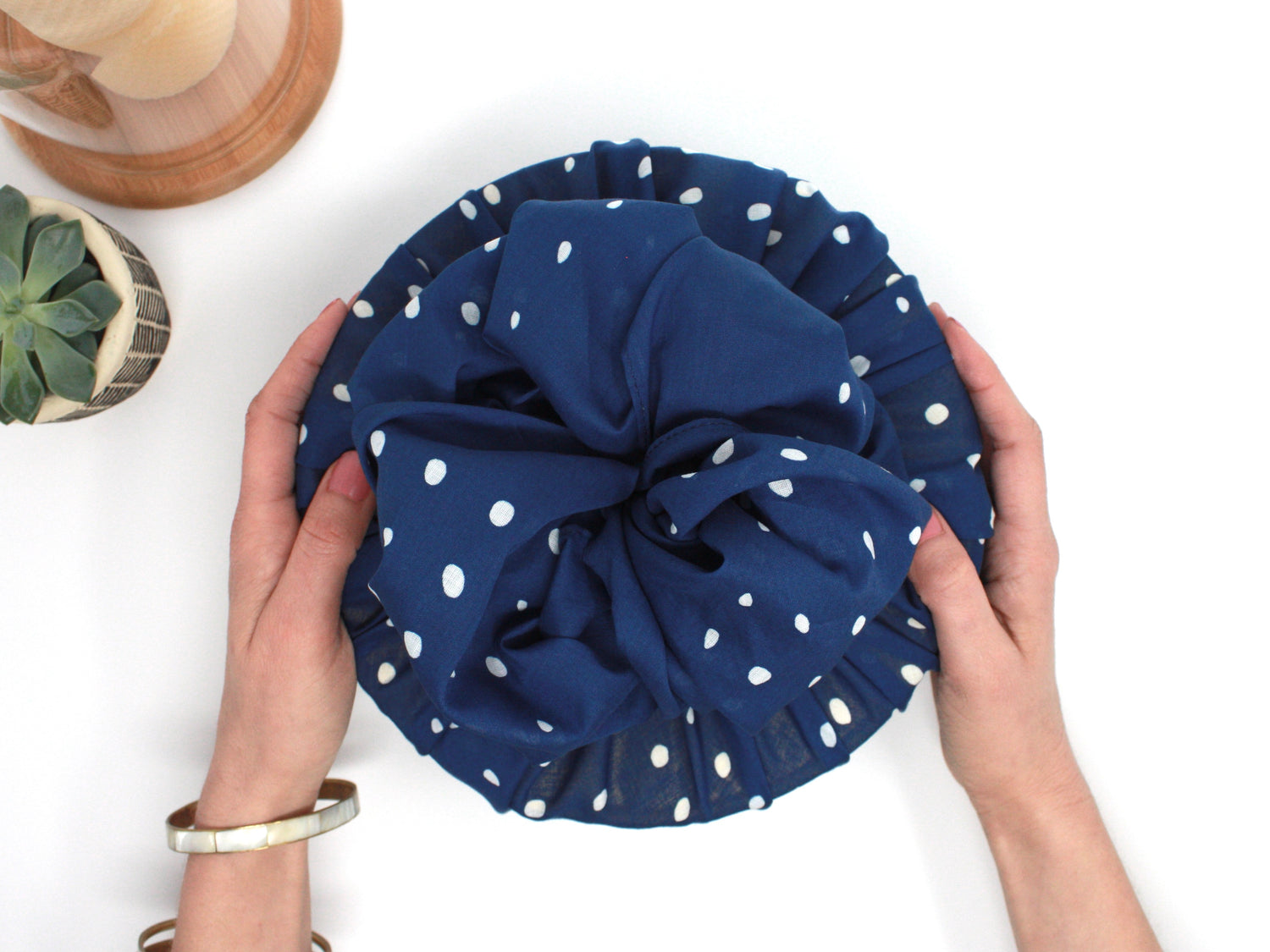 Round gift wrapped in fabric wrapping paper. Two hands are shown giving the gift