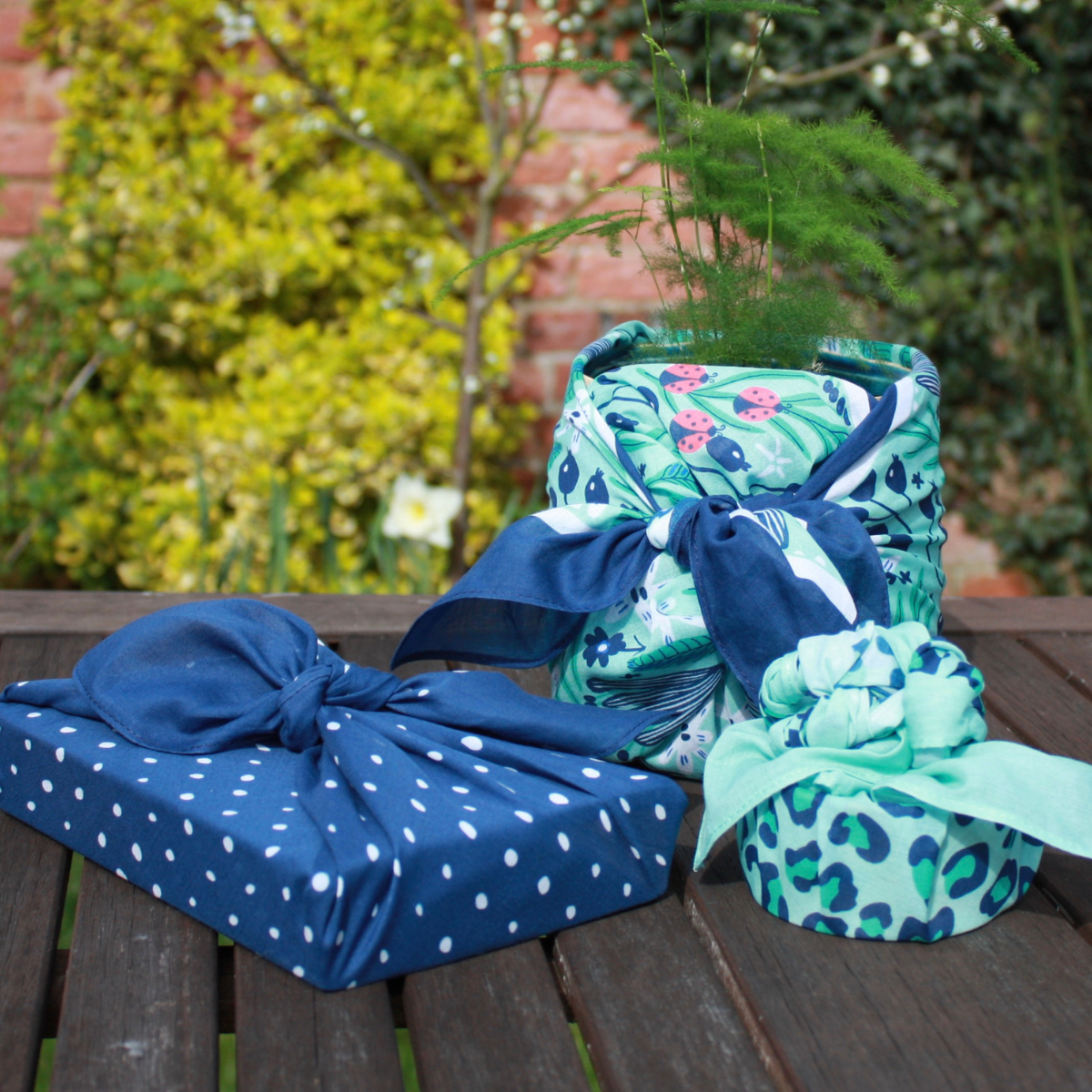 Gifts wrapped in fabric. Three gifts shown all wrapped in fabric, a book, a plant in pot and a trinket dish.