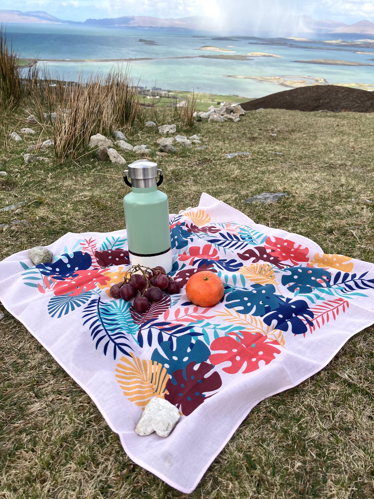 Furoshiki wrap or scarf used as a mini picnic blanket, with a reusable water bottle. Sea and mountains in the distance