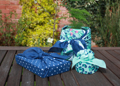 Gifts wrapped in fabric. Three gifts shown all wrapped in fabric, a book, a plant in pot and a trinket dish.